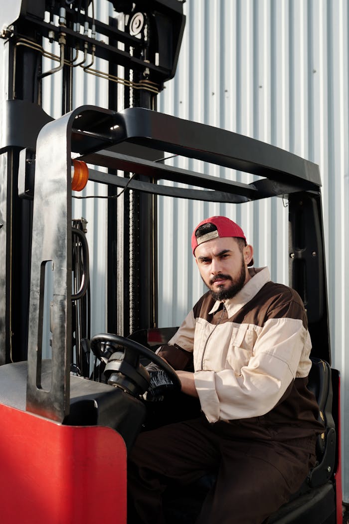 gallery-3 Portrait of a forklift operator inside a warehouse, wearing a uniform and cap.